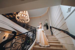 Braut auf eleganter Treppenanlage mit Kronleuchter, Schlosshochzeit Berlin Brandenburg – Spreejuwel Hochzeiten