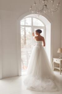Braut im voluminösen Tüllkleid vor Rundbogenfenster von hinten, Hochzeitsplanung Berlin – Spreejuwel Hochzeiten
