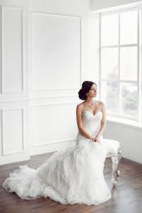 Braut im voluminösen Kleid am Boden vor großem Fenster, elegante Hochzeit Berlin Brandenburg – Spreejuwel Hochzeiten