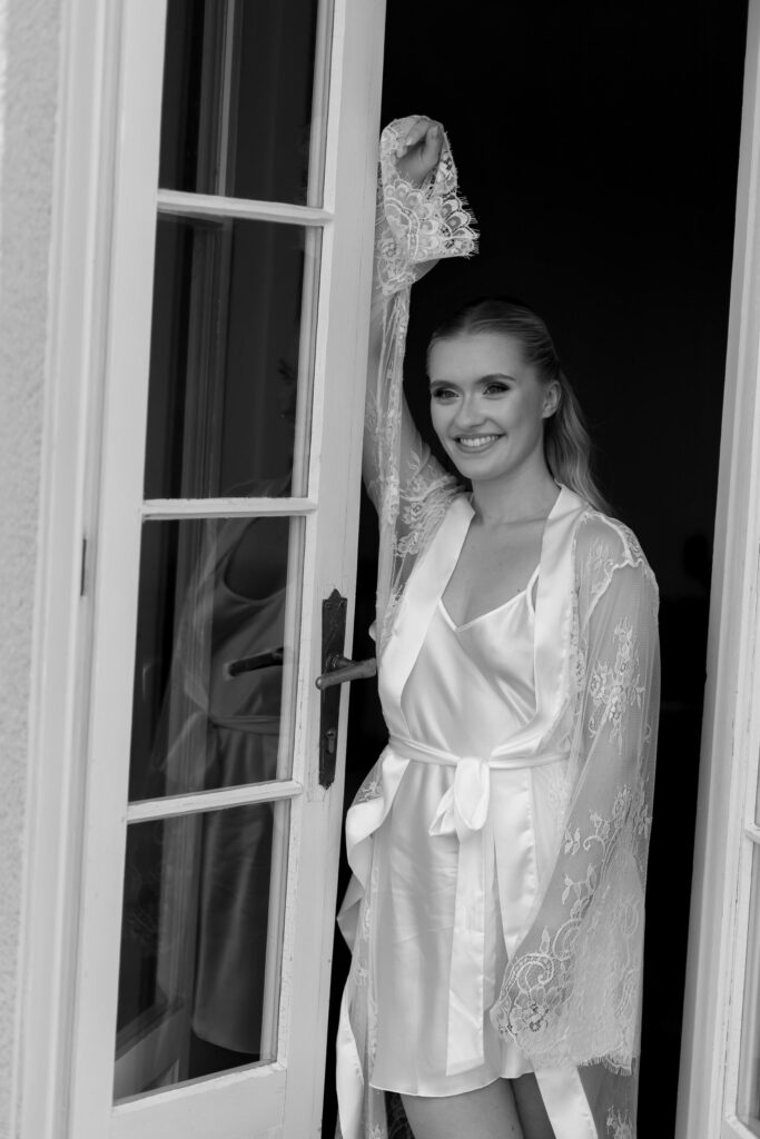 Alt-Text: „Braut im Seidenmorgenmantel beim Getting Ready in der Villa Aurea in Potsdam, Schwarzweiß – Begleitung am Hochzeitstag durch Spreejuwel Hochzeiten