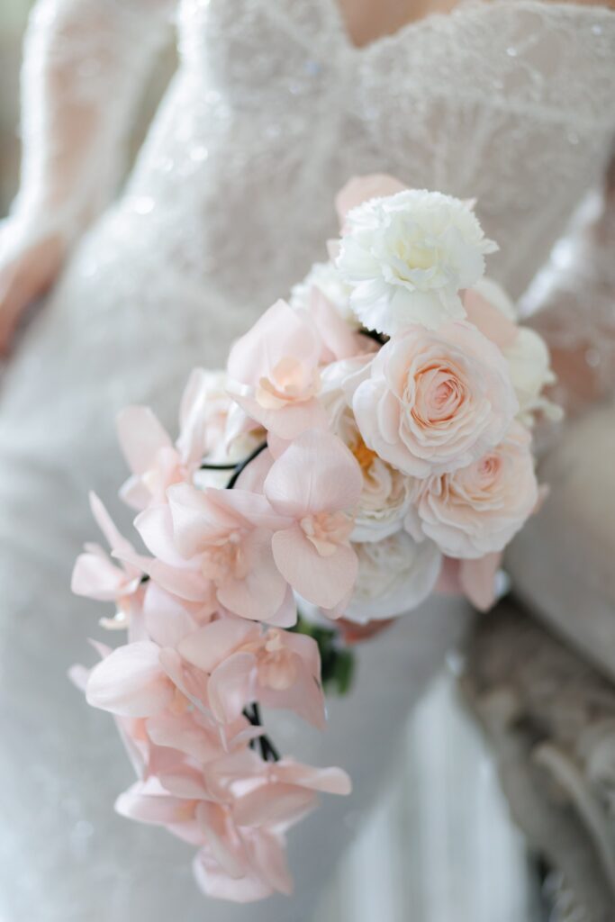Brautstrauß aus Rosen und Orchideen in Blush vor dem bestickten Spitzenkleid der Braut – Komplettplanung durch Spreejuwel Hochzeiten