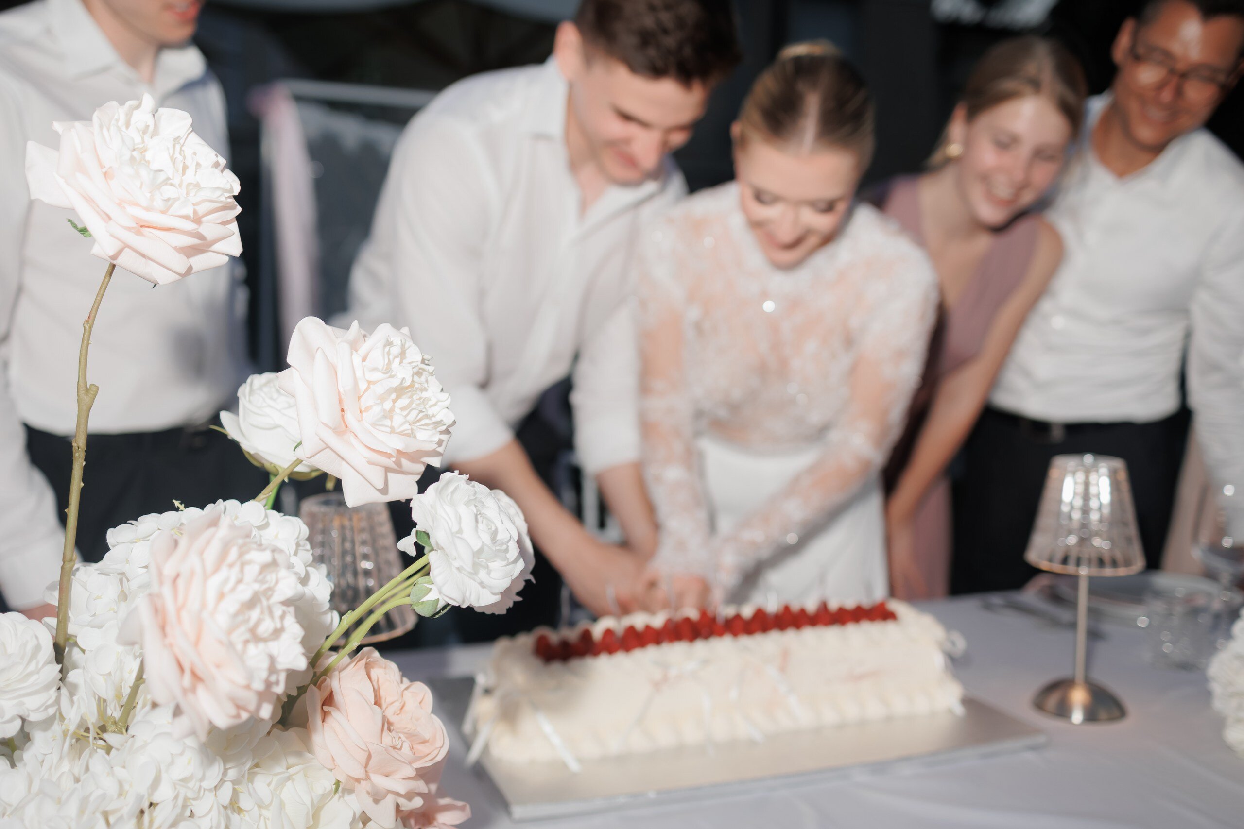 Brautpaar beim Anschnitt der Hochzeitstorte mit Himbeeren, umrahmt von zartrosa Rosen und Hortensien, Hochzeit in der Villa Aurea in Potsdam